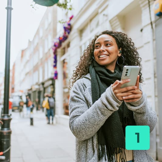 1 - woman walking down street smiling holding phone