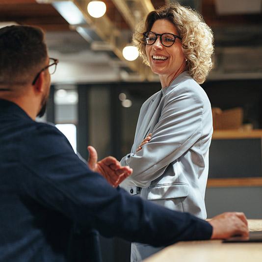 Two colleagues smiling and talking at a desk