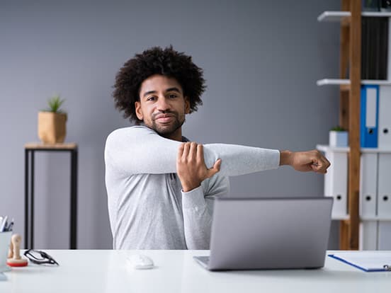 Man stretching his arm whilst sat at a desk