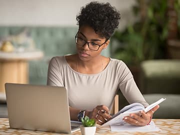 Woman working at home on laptop with paperwork