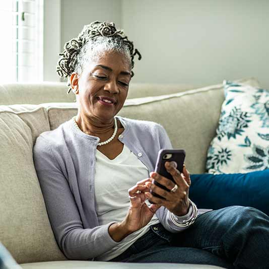 3. An older woman sitting on a couch and using a mobile device