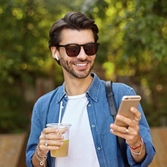 Man wearing sunglasses, smiling at smartphone