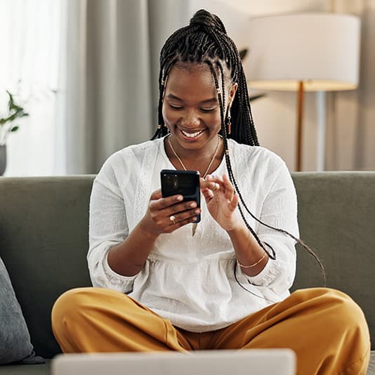 Smiling lady on sofa with mobile phone and laptop