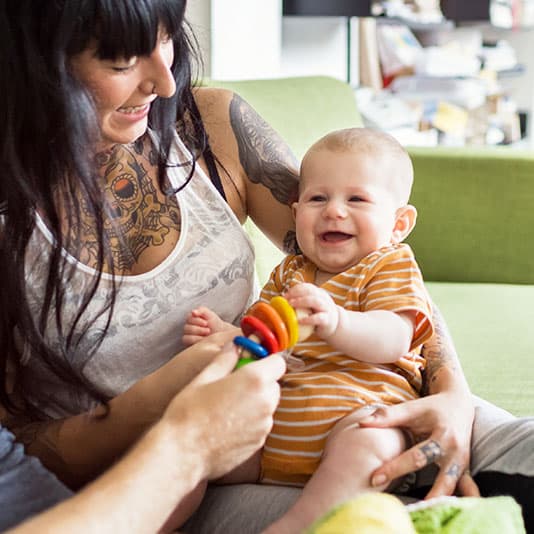 Tattooed mother holding baby with toy