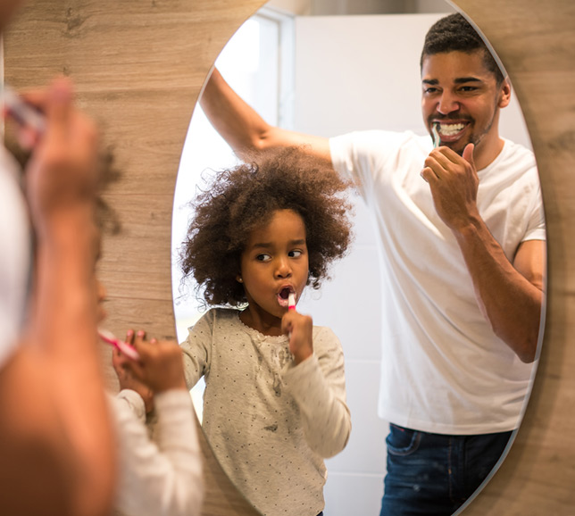 Father and child brushing their teeth together in the mirror