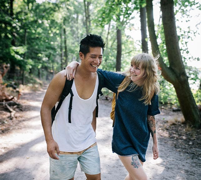 A young couple smiling and walking together along a woodland path